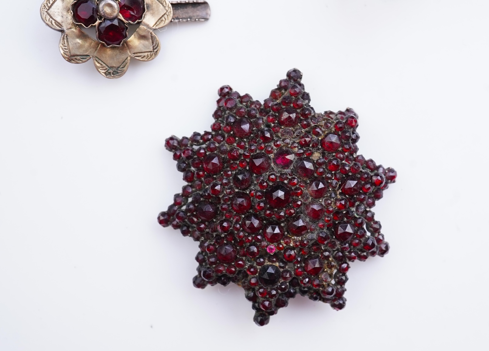 A suite of garnet and paste jewellery, comprising: a brooch, 5cm diameter; a bangle, inner circumference 16cm; two rings, sizes I and M; a pair of earrings, and a single earring, each set with rose-cut garnets; and a pai